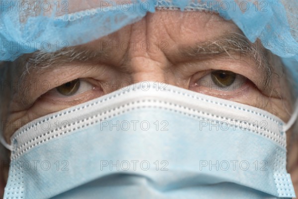 Close up portrait of sad senior adult dressed in surgical face mask with ear straps, covering nose from SARS, virulently infectious disease corona virus. Sad gaze man eyes during pandemic, quarantine