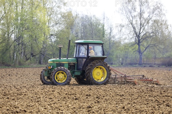 Farmer cultivating field with green John Deere 2140 utility tractor and harrow in the spring. Salo, Finland. May 13, 2021