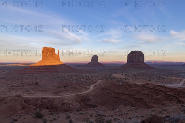 A picture of the Monument Valley landscape at sunset, with the West Mitten Butte, East Mitten Butte and Merrick Butte rock formations in the center
