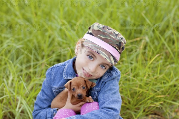 Little girl with pet puppy mascot mini pinscher in outdoor green grass