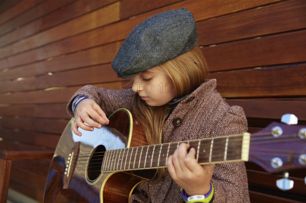 Blond kid girl playing guitar with winter beret and coat on wooden background