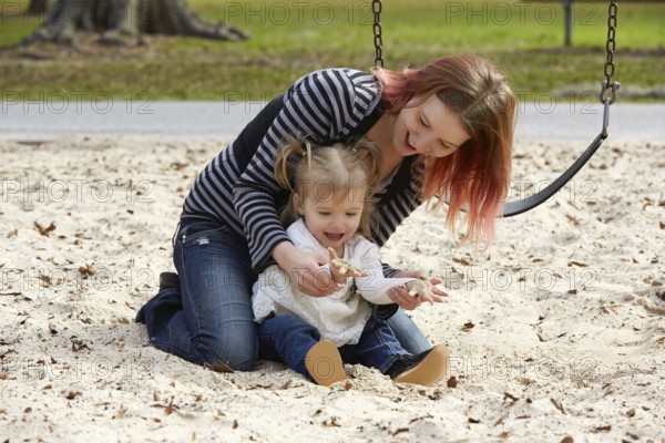 Mother and daughter playing with sand having fun at the park playground