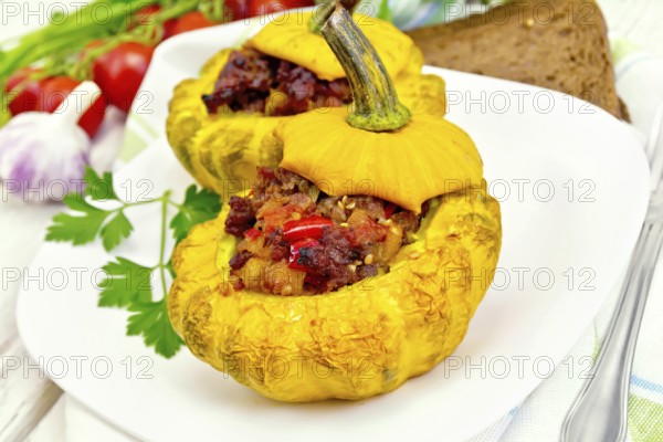 Two yellow squash stuffed with meat, tomatoes and peppers in the dish, bread, garlic, parsley and a napkin on a wooden boards background
