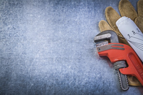 Monkey adjustable wrench protective gloves rolled blueprints on metallic background plumbing concept