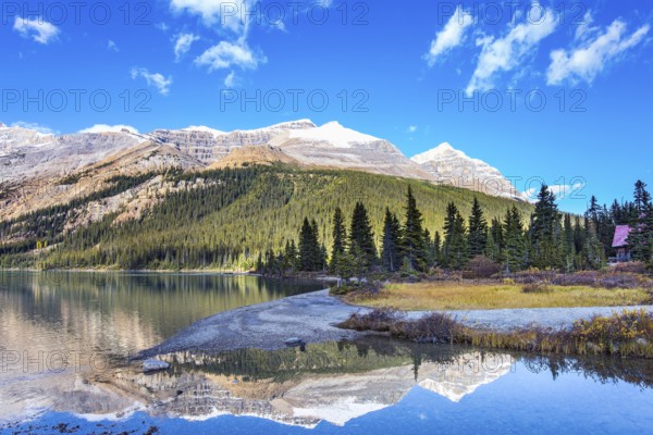 Canada. Rocky Mountains. Sun and mountains are reflected in the smooth water of the lake. Glacial lake Bow with clear azure water. Sunny autumn day
