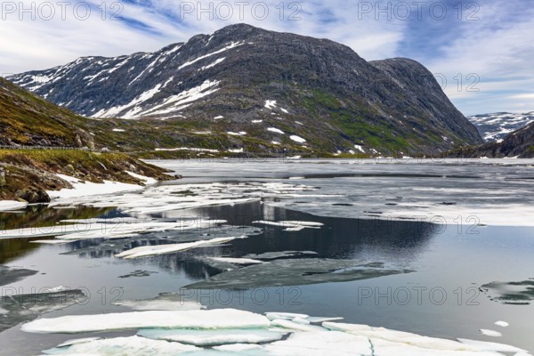 Norway. The cold clear water of the lake Djupvatnet is covered with ice in July. The mountains are covered with freshly fallen snow. Kingdom of the Snow Queen