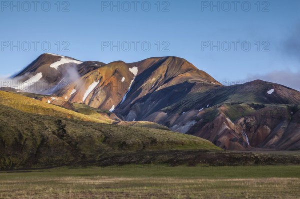 In the hollows of rhyolitic mountain snow. Above the source of hot water steam rises. Early summer morning in the National Park Landmannalaugar, Iceland, Europe