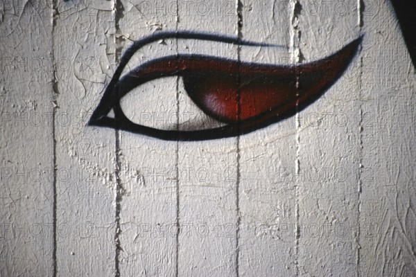 A spray-painted or painted woman's eye with red pupils on a concrete wall
