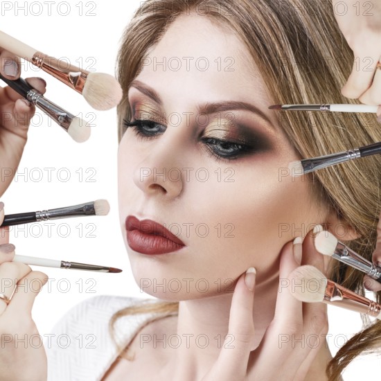 Many hands with cosmetics brushes applying make-up to glamour woman