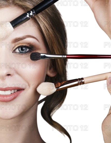 Many hands with cosmetics brushes applying make-up to glamour woman, over white background