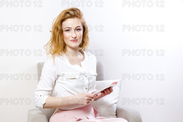 People, technology and education concept - young student woman sitting on a chair and using a tablet on white background