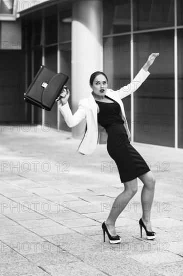 Scared young businesswoman with briefcase and gesturing fear on city background