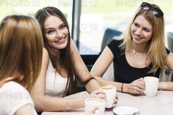 Happy women holding coffee cup while looking at each other in cafe
