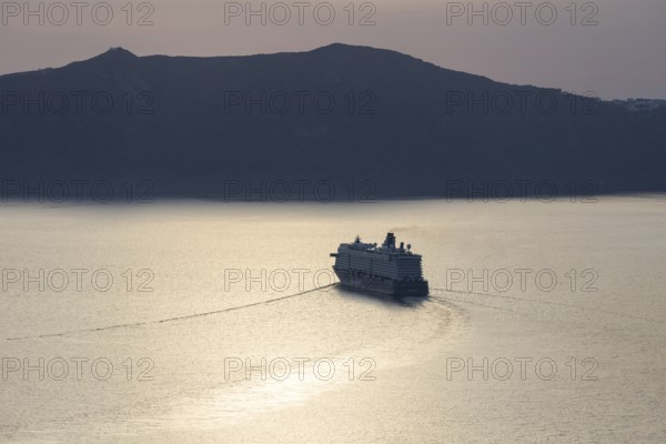 Golden evening light, view from Fira, cruise ship leaving Santorini archipelago, Thirassia island in the background, backlight shot, Santorini island, Cyclades, Greece, Europe