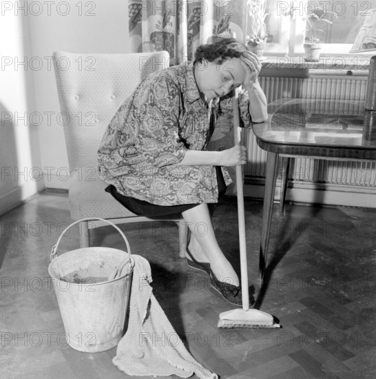 Cleaning the floor back then. A woman looks very tired and worn out when sitting on a chair, having a rest in the work of cleaning the floors. Sweden 1956 Conard ref 3160