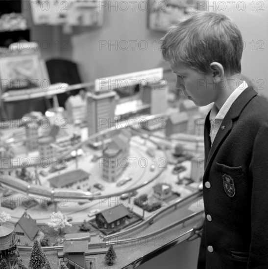 Toys in the 1960s. A boy at a model railway in a store. It's built with buildings and trees and was a popular hobby at the time. The model trains in the picture are made by british Tri-ang railways. Other famous manufacutrers were Märklin and Fleischmann. Sweden 1962
