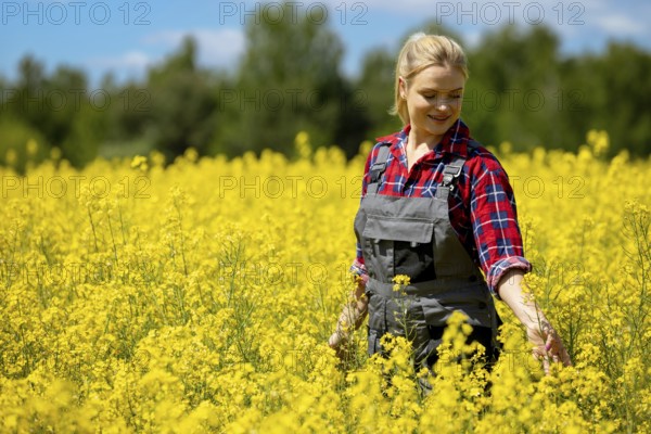 A cheerful woman dressed in denim overalls joyfully explores a vibrant yellow flower field beneath a sunny sky