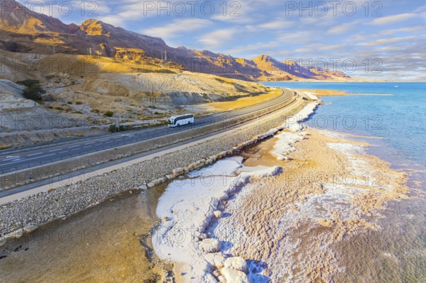 Asphalt highway runs along the seashore. Dead Sea, Israel. Shallowed Dead Sea photographed from a drone. Evaporated salt was deposited along the shore. Evening twilight in winter