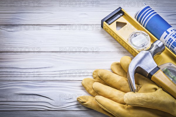 Claw hammer blue rolled construction plans level safety gloves on wooden board