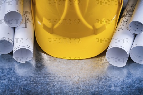 Metallic background with white architectural blueprint rolls and yellow building helmet close up image construction concept
