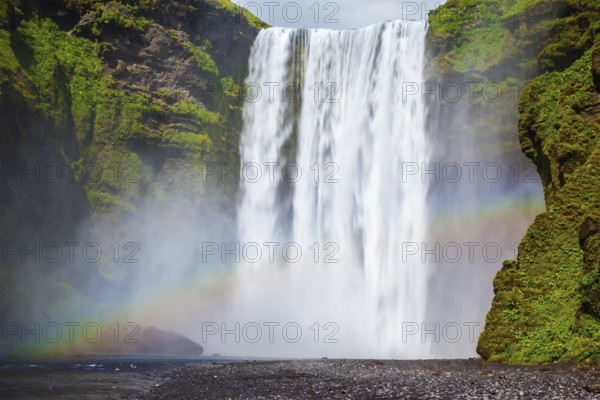 Picturesque rainbow appears in the water mist. The most popular waterfall in Iceland - Skogafoss. Water rushes down with a crash, forming a cloud of mist