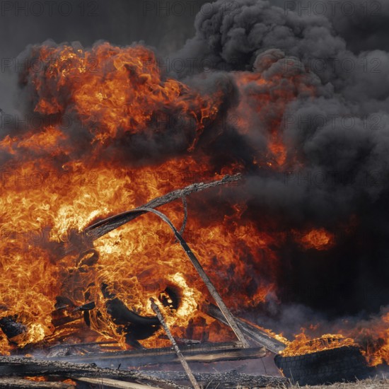 Burning cars tires, strong flame of red-orange fire and clouds of black smoke in sky. Selective focus, blur from strong fire