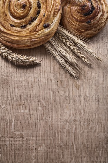 Golden wheat ears raisin baked buns on oaken wooden board food and drink concept