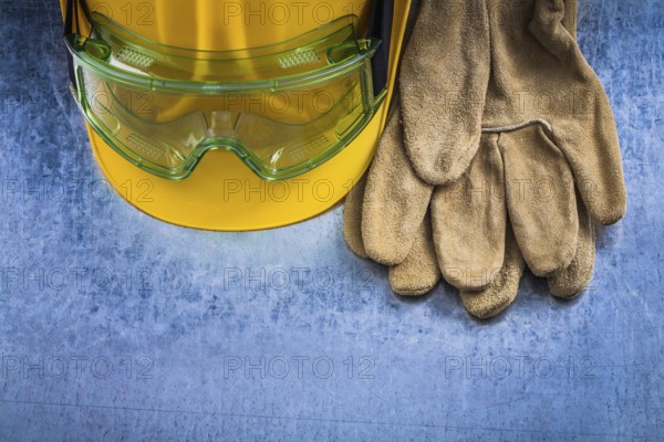 Safety leather gloves hard hat and multiple-purpose protective glasses on scratched metallic background construction concept