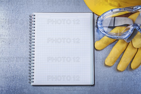 Safety spectacles gloves copybook hard hat on scratched metallic background