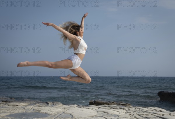 Young woman dancing outdoors on a rocky coast by the sea