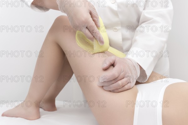 Cosmetologist hands in gloves removing hair on women leg. Depilation procedure with green hot wax in professional beauty salon. Part of photo series