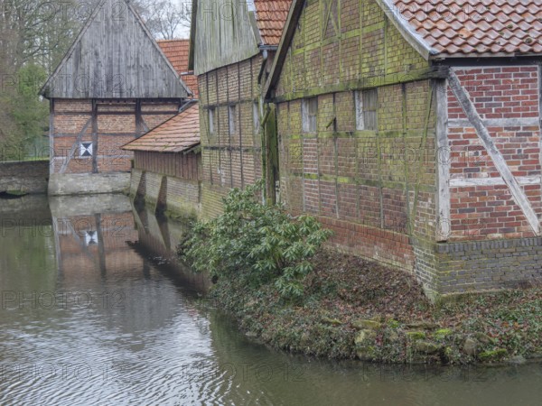 Half-timbered houses with red bricks by the water, surrounded by winter vegetation, aulendorf, münsterland, germany
