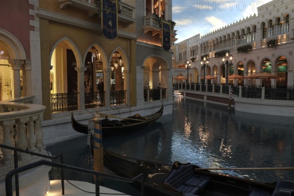 An attraction inside The Venetian hotel: gondolas on a canal lined with typical Venetian-style houses with arcades, balconies and columns. Above them is an artificial sky that simulates the times of day with changing daylight in a shortened time sequence. One of the attractions inside the hotel The Venetian: Gondolas on a channel which is bordered by typical houses with arcades and balconies in the Venetian style. About it an artificial sky that simulates the time of day