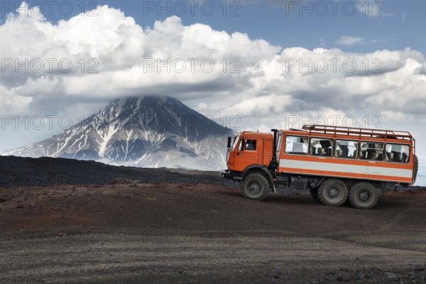 KAMCHATKA, RUSSIA, JUNE 24, 2016: Russian expedition truck KamAZ (6-wheel drive) on mountain road on background of lava fields and beautiful volcano. Eurasia, Russian Federation, Far East, Kamchatka Peninsula, Klyuchevskaya Group of Volcanoes