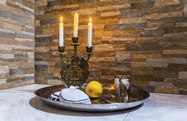 Beautiful candlestick with burning candles, a silver glass for blessing and a white yarmulke. Background stone wall. Still life with objects Judaica. Concept of artistic photography