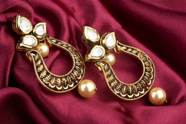 Beautiful Golden pair of earrings Diamonds gemstones on a red satin background. Luxury female jewelry, Indian traditional jewellery, kundan earring, Bridal Gold earrings wedding jewellery
