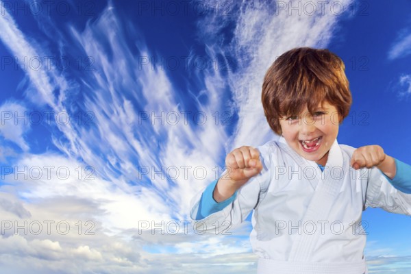 Concept - photo advertising, children, sports. Boy in a white kimono practices judo. Background - blue sky and flying cirrus clouds