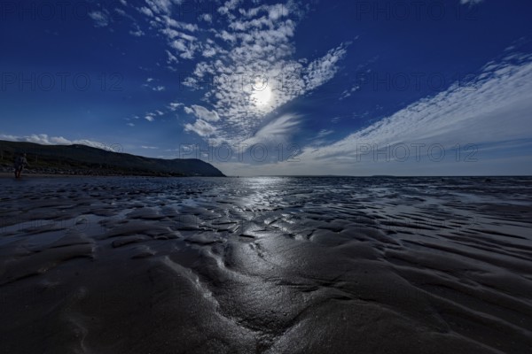 Dimly lit beach with dramatic sky and sparkling sea on the edge of Snowdonia National Park, Penmaenmawr, Dwygyfylchi, Caernarfonshire, Conwy County Borough, Wales, United Kingdom, Europe