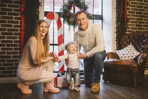 Theme of Christmas holidays and New Year mood. Family posing at home near christmas decor on christmas evening. Three mom dad and son in the winter at the window