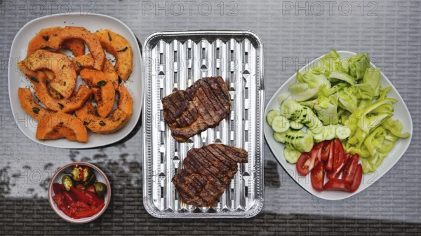 Grilled butternut squash and pork cuts, some fresh vegetable next to it, on glass garden table, view from above, Pribylina, Slovakia, Europe
