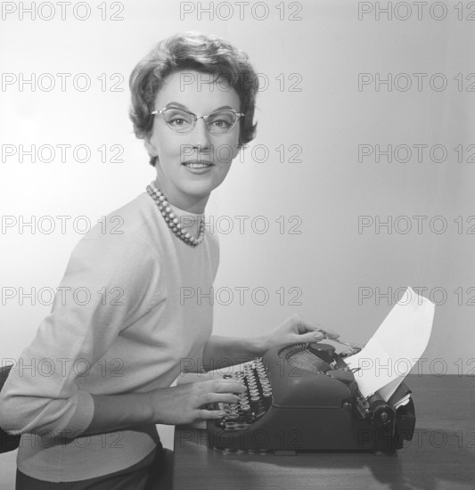 Office girl in the 1950s. A young girl at her typewriter is wearing typical fifties glasses and jumper. 1950s. Photo Kristoffersson/CB96-10