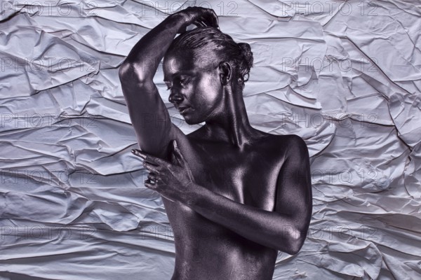 Young beautiful naked woman with glossy skin is posing on the crumpled paper background