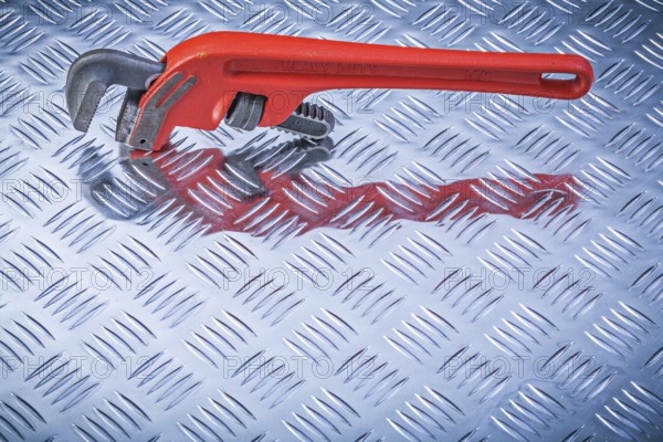Metal pipe wrench on corrugated metallic background directly above maintenance concept