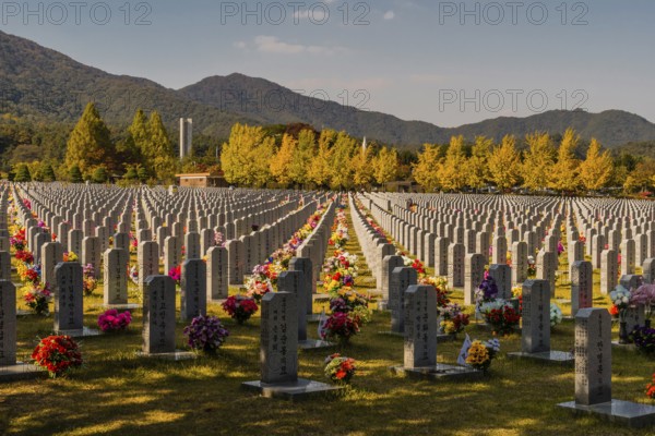 Daejeon, South Korea, October 27, 2019: War memorial and hercules missile above trees in fall colors behind field of headstones at National Cemetery, Asia