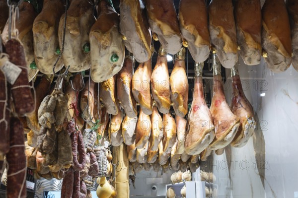 Large hams and other cold cuts hanging in an Italian shop