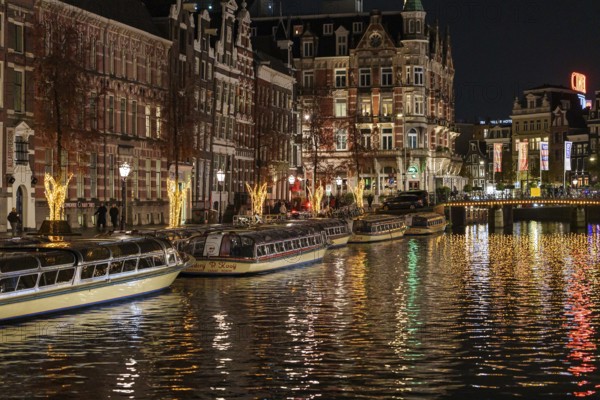 A night-time view of the canal with illuminated boats and imposing buildings, Amsterdam, Netherlands