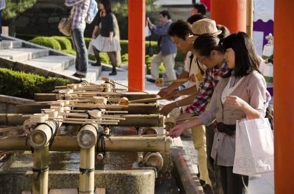 People washing hands at a Tsukubai in front of the Inari Shrine in Kyoto in order to purify themselves by the ritual washing, Kyoto, Japan, Asia