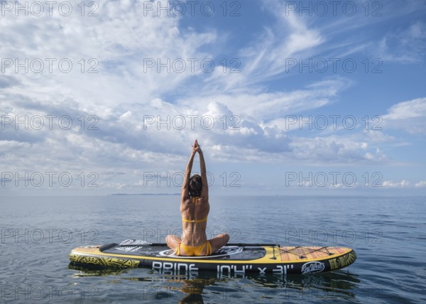 Woman practicing yoga on a surfboard under a dramatic sky, Estalella, coast of Llucmajor, Majorca, Balearic Islands, Spain, Europe