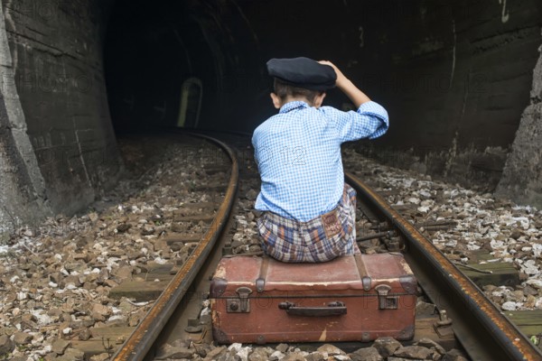 Child in vintage clothes sits on railway road in front of a tunnel