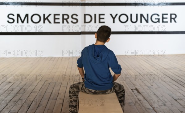 Teenager smoking and message on wall - Smokers die younger. No smoking concept with child. Casual clothes